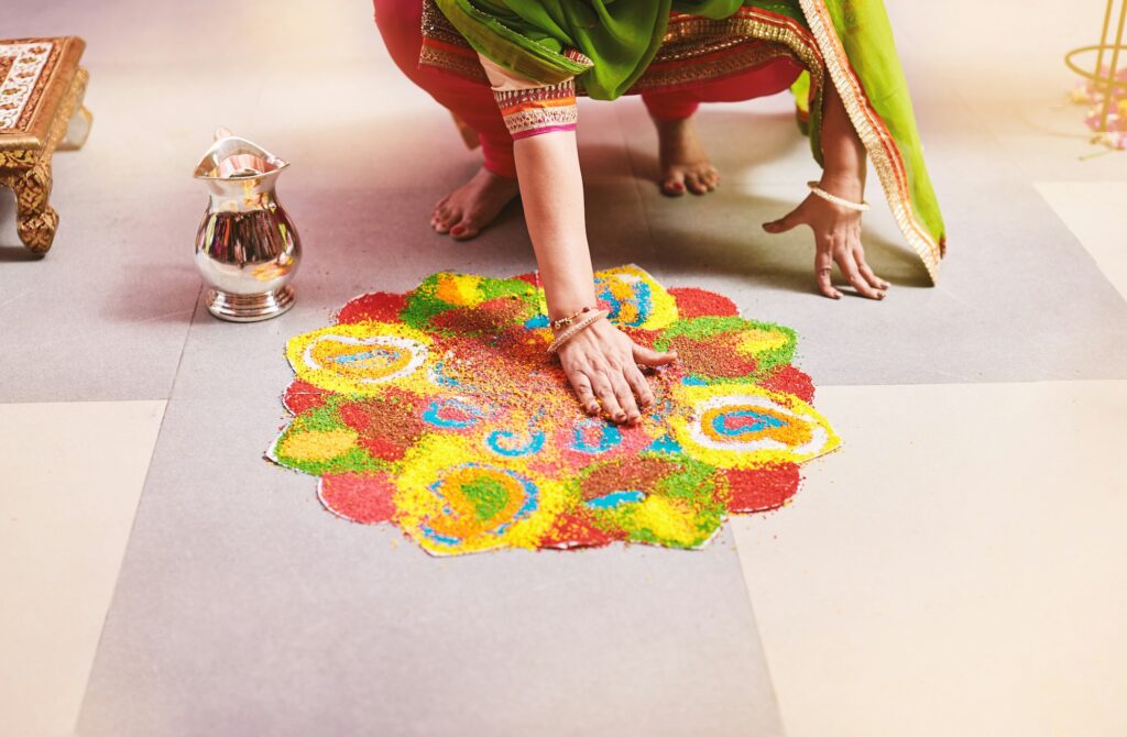 Women coloring tradition colorful rice art or sand art (Rangoli) on the floor with paper pattern